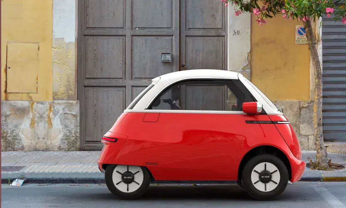 Un triciclo y cuadriciclo de motor rojo y blanco, un vehículo eléctrico compacto, estacionado frente a una puerta de madera y una pared amarilla.