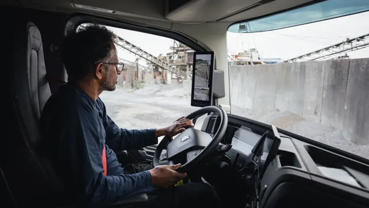 Interior de un camion Volvo. Un hombre con gafas conduce, observando las cámaras de visión.