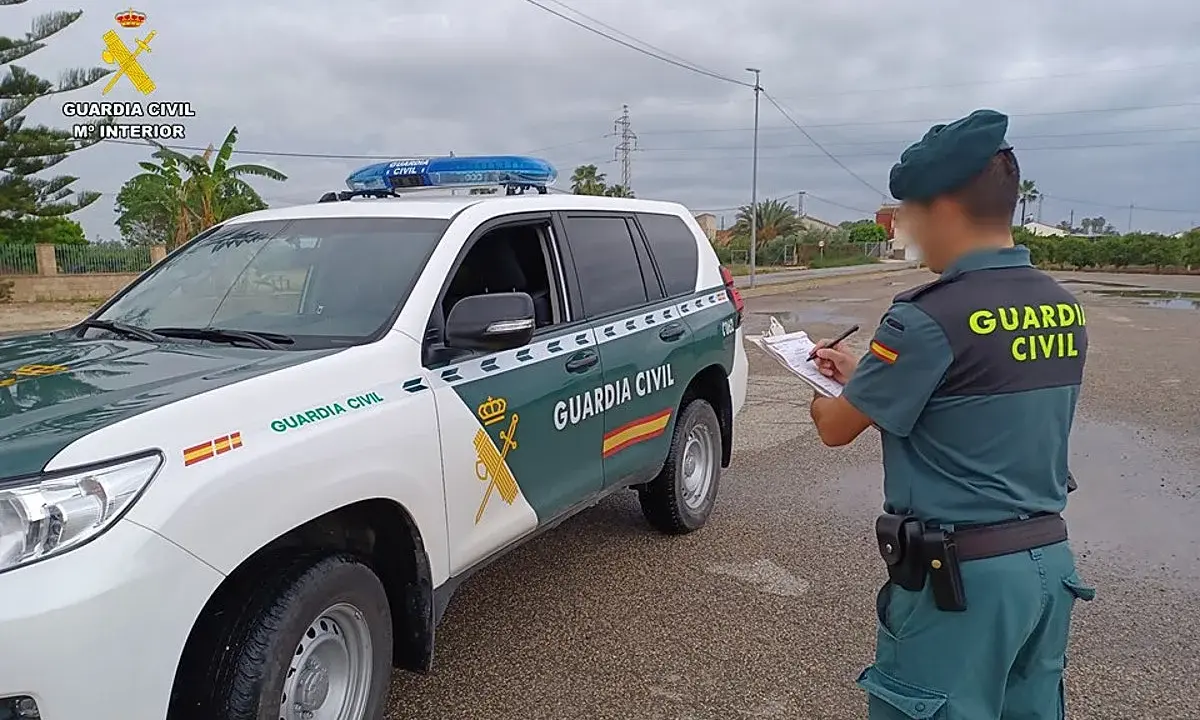 Agente de la Guardia Civil anota datos junto a un vehículo oficial. Se pregunta qué carnet se necesita para conducir un minibus.