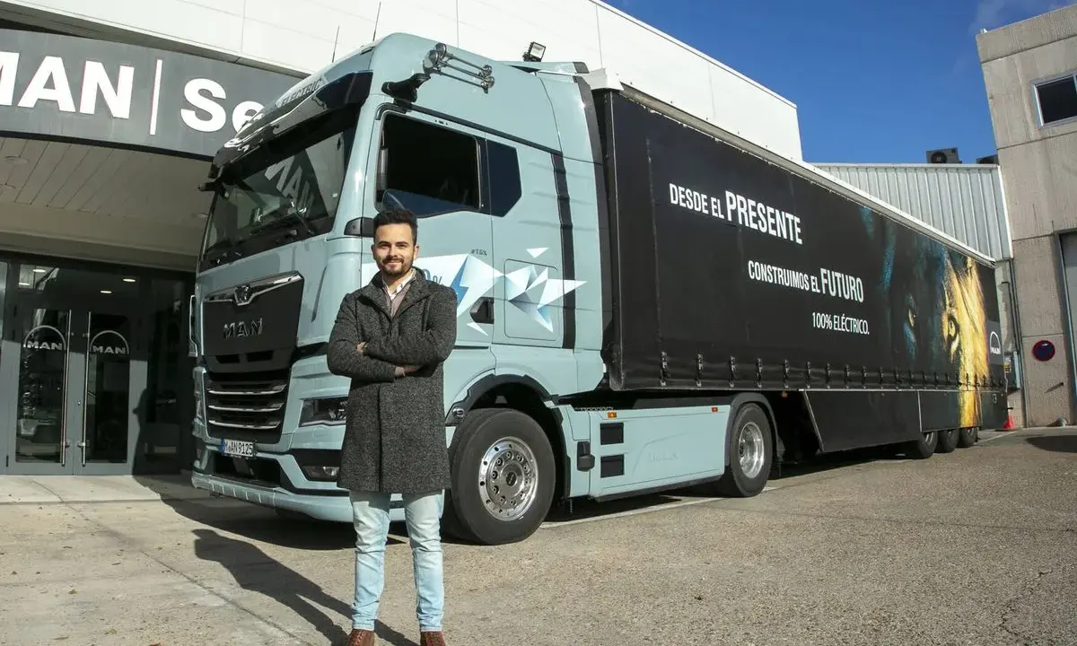 Hombre posa frente a un camión eléctrico MAN, como en las revistas de camiones. El remolque tiene un león y el lema "Construimos el futuro".