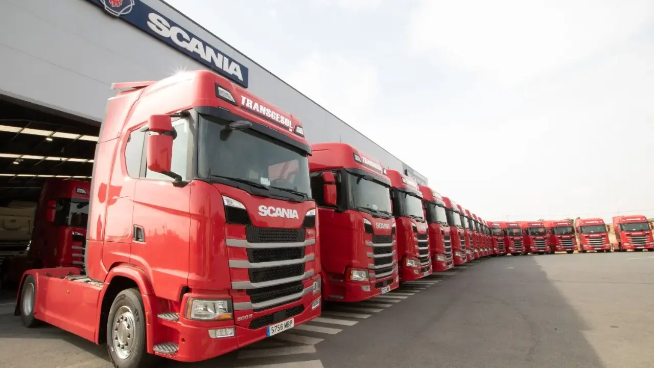 Una fila de camiones Scania rojos, listos para la acción, con el logo de Scania en el edificio.