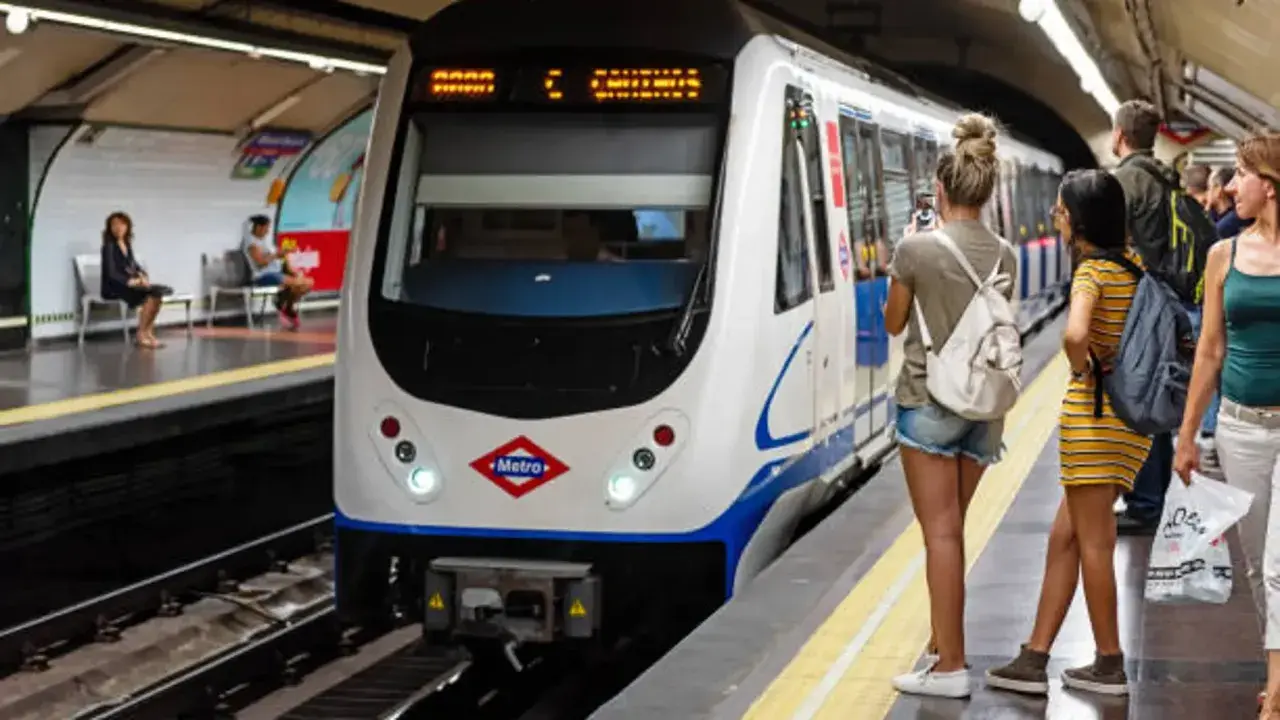 En la estación de metro, un tren blanco espera. Varias personas observan, una podría recibir una multa por usar tarjeta de transporte de otra persona.