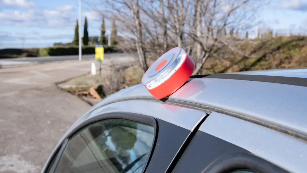 Baliza de emergencia roja y blanca en el techo de un coche plateado, lista para evitar una multa.