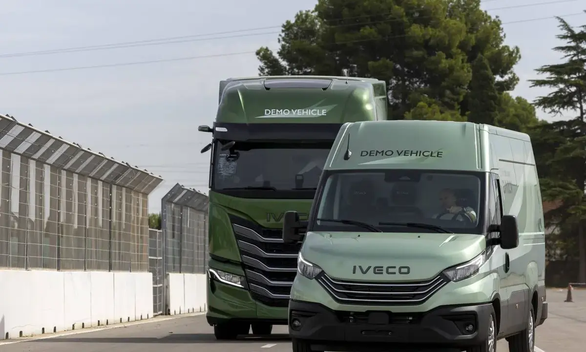 Dos vehículos Iveco, un camión y una furgoneta, ambos de color verde y con la etiqueta "DEMO VEHICLE", circulan por una carretera.
