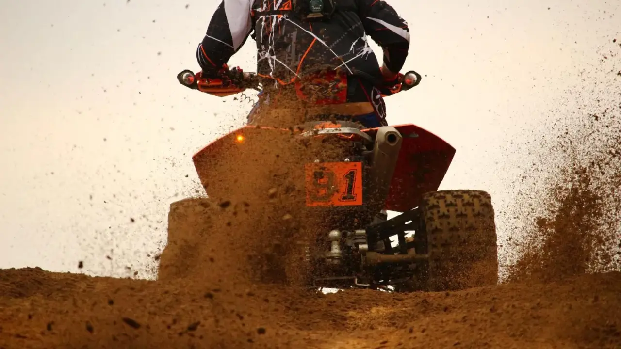 Un quad naranja con el número 1 salpica barro a máxima velocidad.
