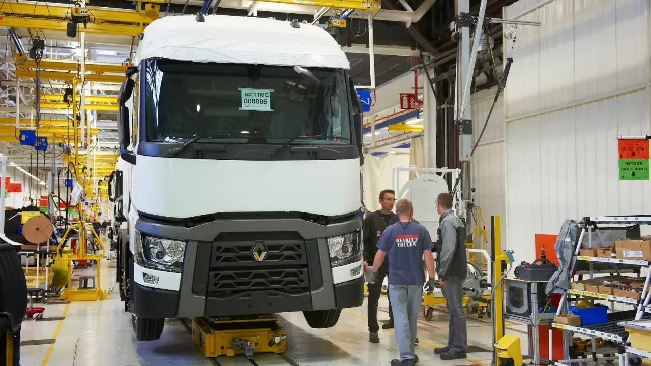 Tres trabajadores observan un camión Renault en una línea de montaje. El camión está sobre una plataforma amarilla.
