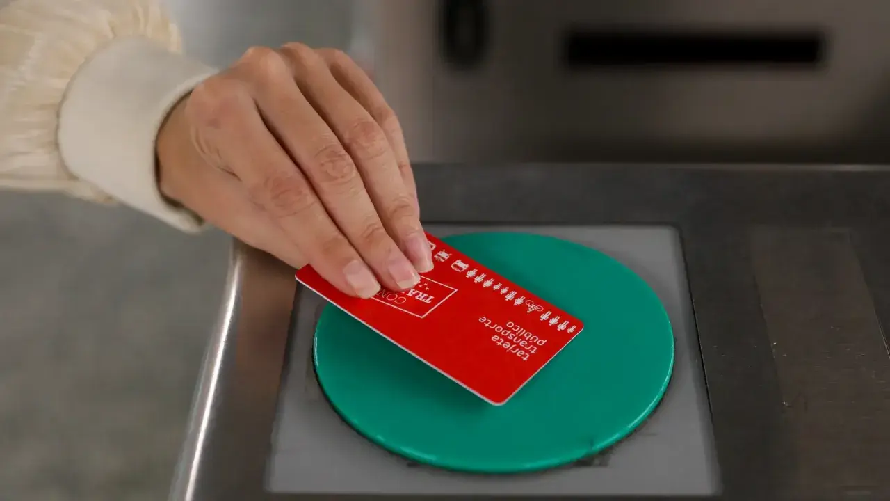 Mano acercando tarjeta roja de transporte público a un lector verde.