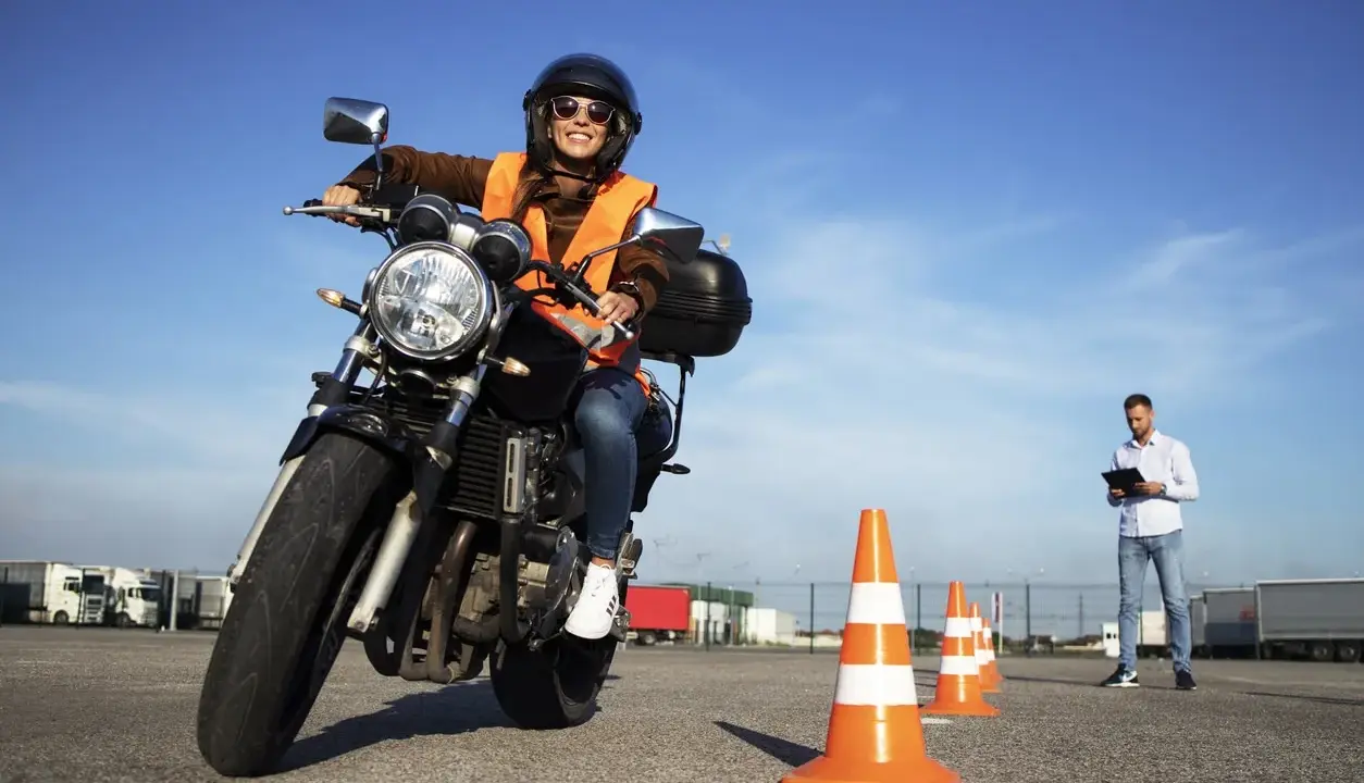 Mujer sonriente practica en circuito cerrado a1, con conos naranjas y un instructor al fondo.