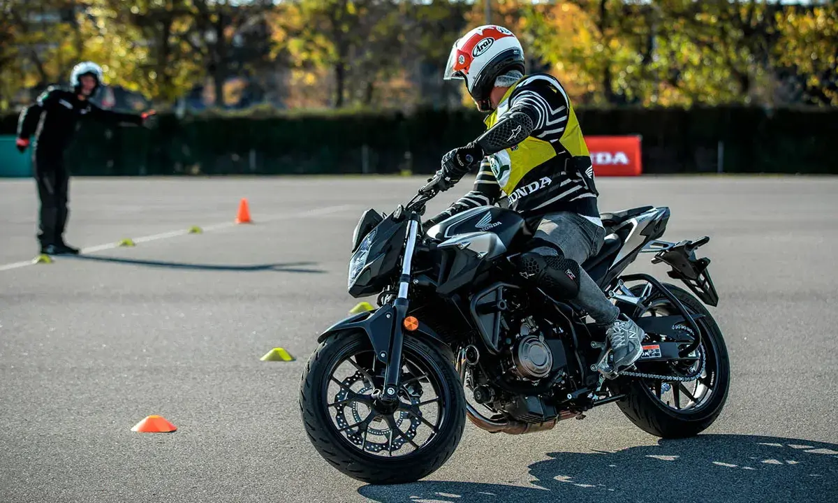 Motociclista con equipo de protección en una pista de examen con conos.