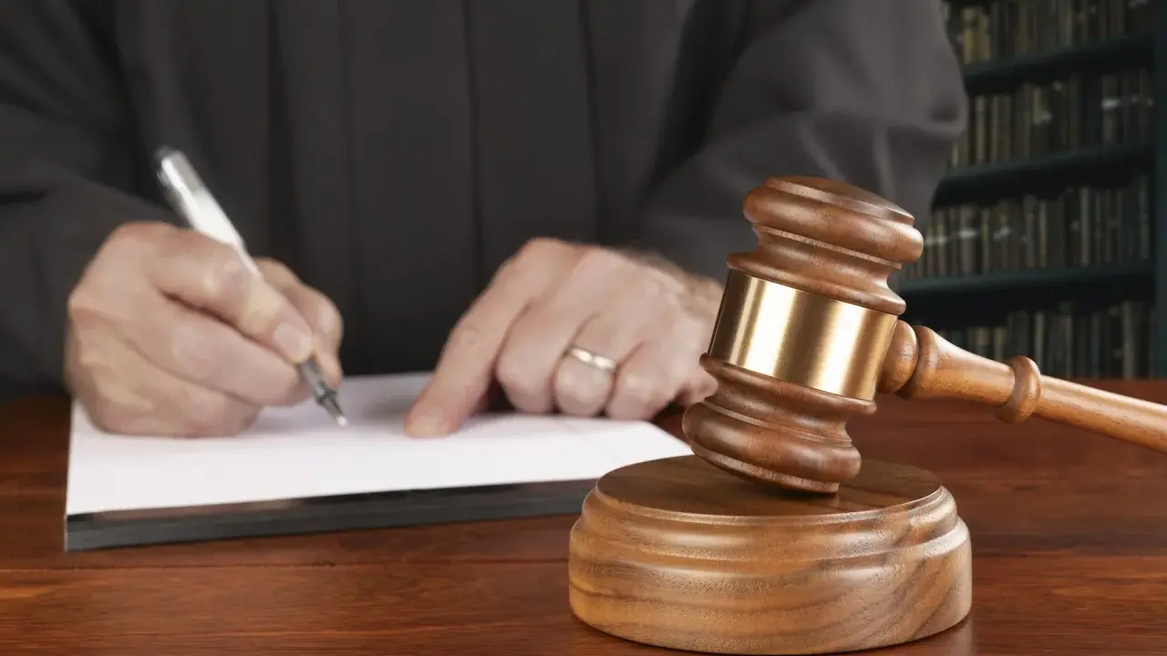 Juez firma sentencia que implica retirada carnet de conducir por curso. Martillo de juez y libros de derecho.