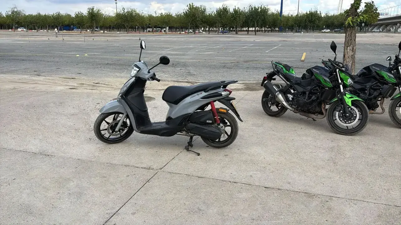 Un carnet scooter gris y dos motos verdes aparcadas en un circuito.