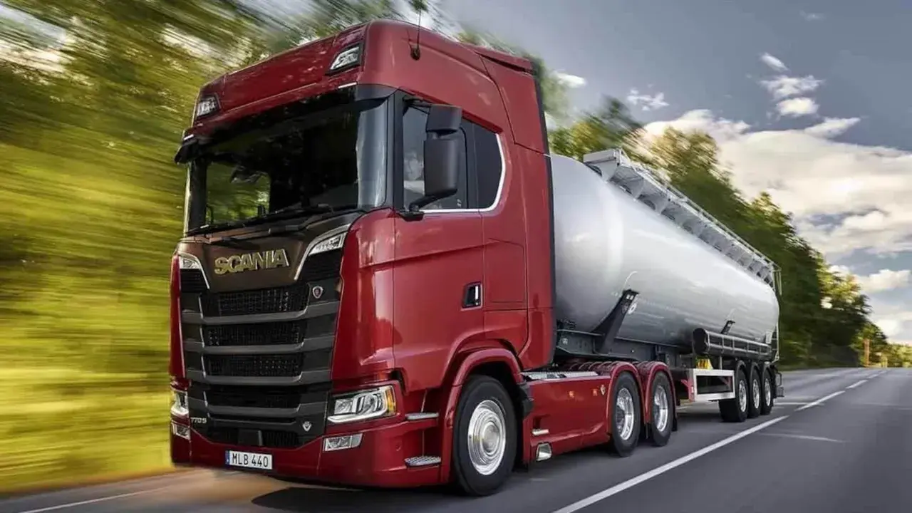 Camión cisterna Scania 800 CV de color rojo brillante, circulando por una carretera rodeada de árboles.