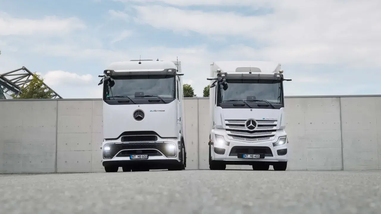 Dos camiones Mercedes-Benz eActros blancos, un nuevo camión eléctrico, se exhiben frente a un muro de hormigón.