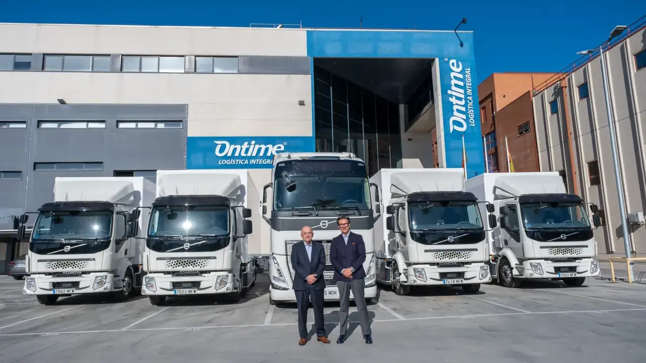 Dos hombres posan frente a una fila de camiones eléctricos de Ontime.