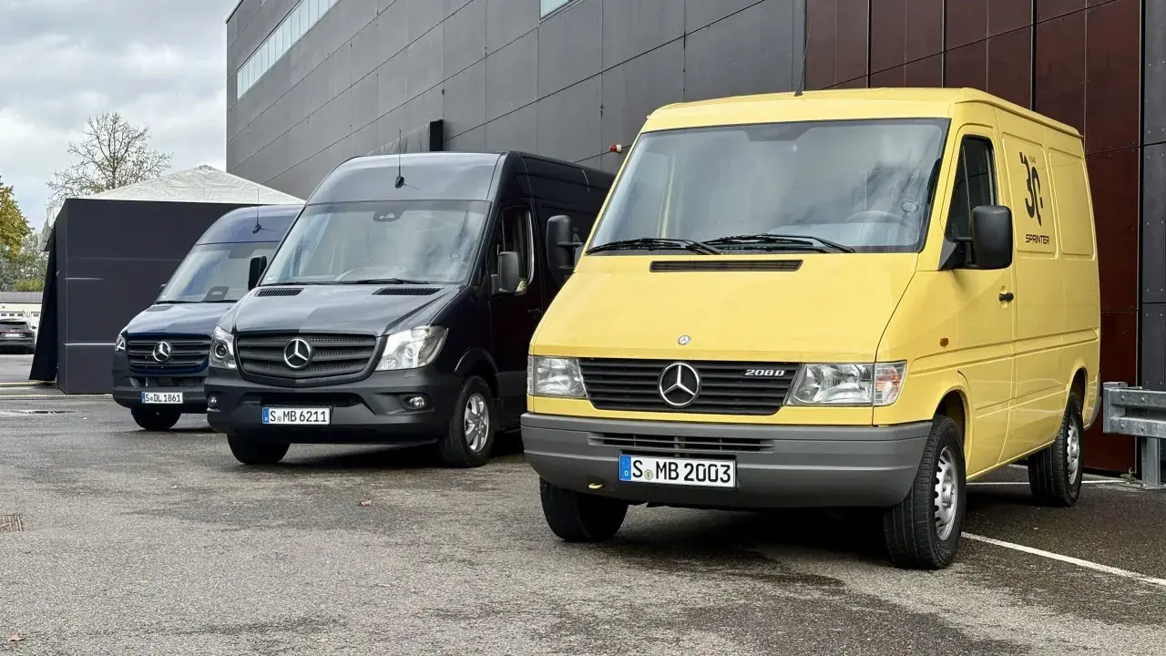 Tres furgonetas Mercedes-Benz Sprinter, una amarilla conmemorativa de 30 años, una negra y una azul, aparcadas frente a un edificio moderno.