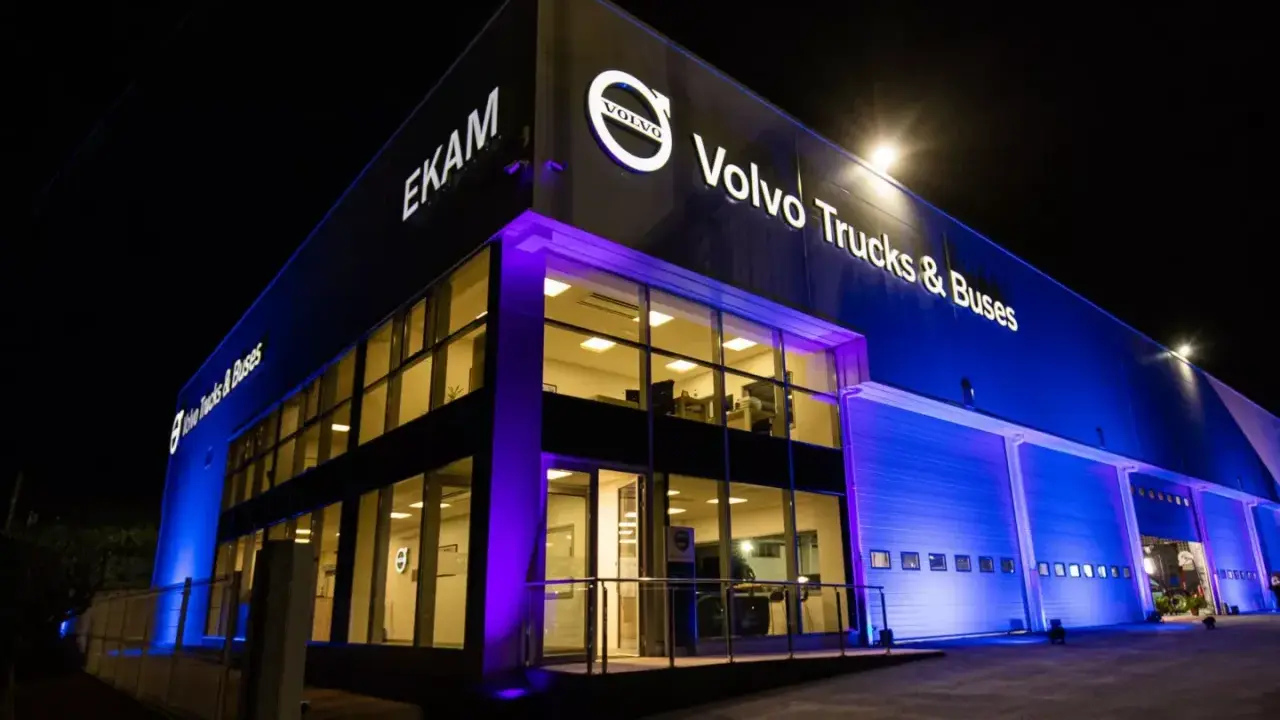 Edificio moderno de EKAM Volvo Trucks & Buses iluminado de noche con luces azules y púrpuras.