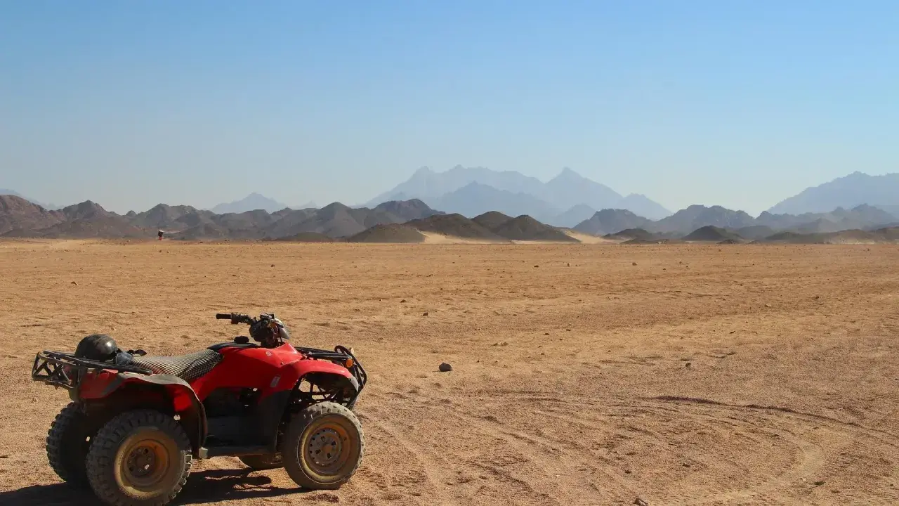 Un quad rojo, listo para la aventura, descansa en el desierto. El carnet para conducir quad 660 es tu pase a la emoción. Montañas distantes y cielo azul completan la escena.