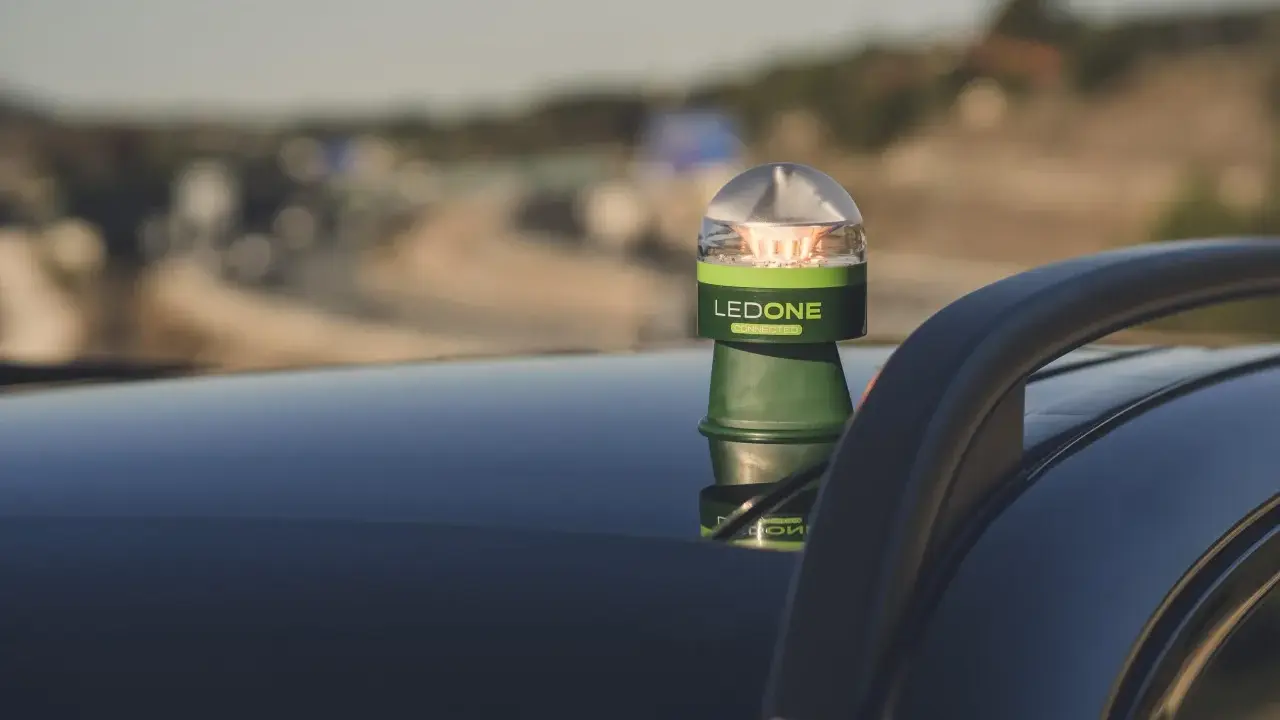 Baliza LED verde y plateada, modelo LEDONE CONNECTED, sobre el techo de un coche. Es una preseñalización de peligro para advertir en carretera.