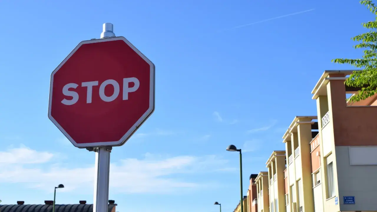 Señal de STOP roja en un poste, con edificios y cielo azul. Indica cómo hacer un stop sin visibilidad.