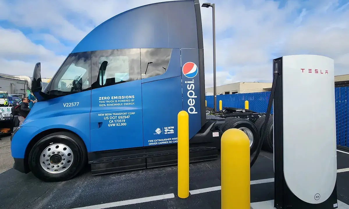 Camión semirremolque azul Pepsi junto a un cargador Tesla.