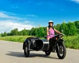 Mujer sonriente con casco blanco conduce una motocicleta negra con sidecar. El permiso A1 autoriza a conducir motocicletas con sidecar.