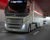 Camión Volvo FH Globetrotter plateado avanza por un túnel con luces rojas. El camión, que parece ser un modelo i-Save, transporta una carga con un diseño hexagonal.