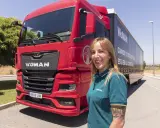 Mujer sonriente junto a un camión rojo MAN TGX. Averigua cuanto cuesta el carnet C+E para conducir este vehículo.