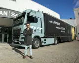 Hombre posa frente a un camión eléctrico MAN, como en las revistas de camiones. El remolque tiene un león y el lema "Construimos el futuro".