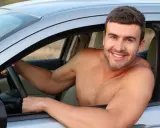 Hombre sonriente al volante de un coche, disfrutando de la libertad de que se puede conducir sin camiseta en un día caluroso.