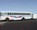 Autobús blanco con franjas azules y rosas, remolcando un tráiler. Ideal para un viaje largo con el carnet D+E.