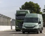 Dos vehículos Iveco, un camión y una furgoneta, ambos de color verde y con la etiqueta "DEMO VEHICLE", circulan por una carretera.