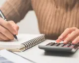 Calculando el precio de clases de conducir. Mano con bolígrafo en cuaderno y otra mano en calculadora.