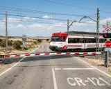 Un tren de carretera de Renfe cruza un paso a nivel con barreras rojas y blancas bajadas. El semáforo está en rojo.