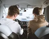 Dos hombres en un coche, uno conduce y el otro mira. Podrían estar discutiendo los tipos de faltas que se cometen al volante.