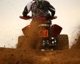 Un quad naranja con el número 1 salpica barro a máxima velocidad.