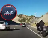 Un motorista de los Mossos d'Esquadra circula por el arcén de una autopista, adelantando a otros vehículos en un día soleado.