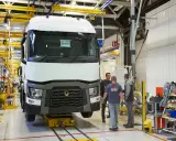 Tres trabajadores observan un camión Renault en una línea de montaje. El camión está sobre una plataforma amarilla.