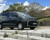 Vehículo mixto gris oscuro aparcado en escalones de piedra con vegetación. Al fondo, escaleras con grafitis y edificios.