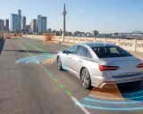 Un coche plateado en una autopista urbana, con gráficos que muestran sus **sistemas de ayuda a la conducción** detectando otros vehículos y obstáculos.