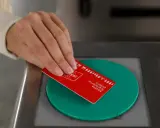 Mano acercando tarjeta roja de transporte público a un lector verde.