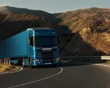 Camión Scania azul recorre una carretera sinuosa entre montañas áridas, evocando la fuerza y el espíritu de aventura de Suecia.