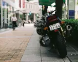 Una moto Yamaha aparcada en la acera, con dos cascos colgados. Al fondo, gente pasea por la calle.