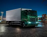 Camión Iveco S-Way V8 780 verde brillante aparcado en un muelle urbano de noche, con luces de ciudad al fondo.