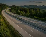 Autopista en Eslovenia, con colinas verdes y árboles. El sol se pone, proyectando sombras largas sobre la carretera. Los **peajes eslovenia** son parte de este paisaje.