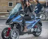 Mujer ajustándose el casco en una moto de 3 ruedas azul, ideal para conducir con carnet B.