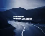 Carretera sinuosa bajo un cielo azul oscuro, con el texto "MICHELIN CONNECTED FLEET" iluminado.