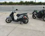 Un carnet scooter gris y dos motos verdes aparcadas en un circuito.