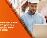 Operador de transporte con casco blanco revisa datos en laptop en almacén. Texto: "5 consejos claves para mejorar la logística de tu empresa".