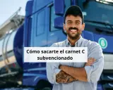 Hombre sonriente con tatuajes, frente a un camión cisterna azul. Aprende cómo obtener tu carnet de camión gratis para desempleados.