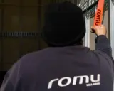 Persona con gorro negro ajusta una cinta naranja con el logo "romu", evitando una multa por exceso de peso.